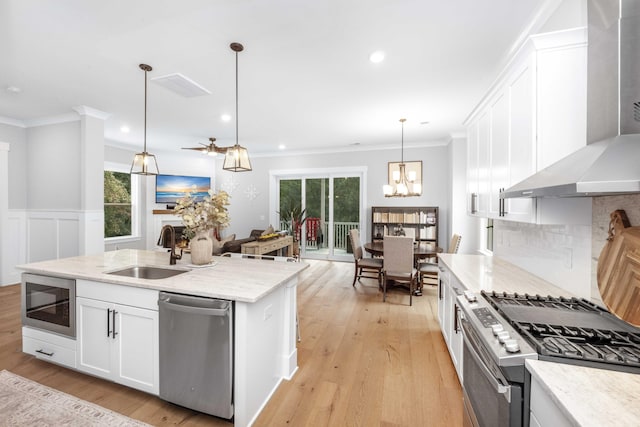 kitchen featuring stainless steel appliances, sink, wall chimney range hood, white cabinetry, and decorative light fixtures