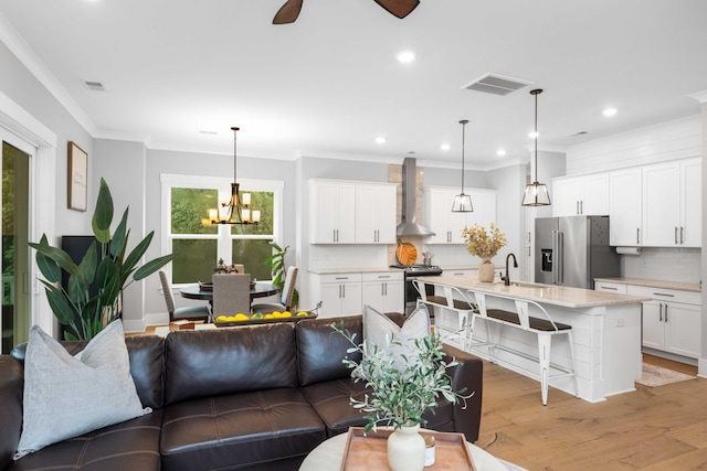 living room with ornamental molding, light wood-type flooring, ceiling fan with notable chandelier, and sink