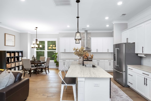 kitchen featuring sink, high quality fridge, a kitchen island with sink, wall chimney range hood, and pendant lighting