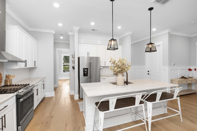 kitchen with stainless steel appliances, white cabinetry, decorative light fixtures, an island with sink, and light wood-type flooring