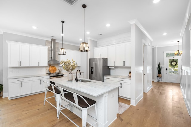 kitchen featuring wall chimney range hood, appliances with stainless steel finishes, decorative light fixtures, light wood-type flooring, and sink