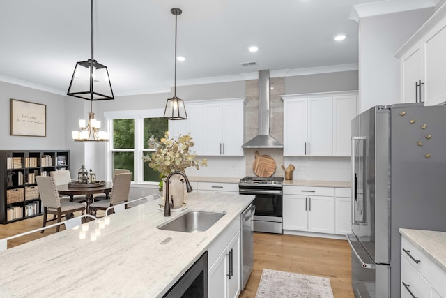 kitchen featuring stainless steel appliances, white cabinetry, sink, decorative light fixtures, and wall chimney range hood