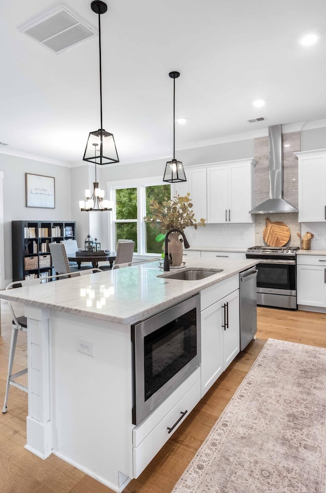 kitchen with white cabinets, stainless steel appliances, a center island with sink, and wall chimney range hood