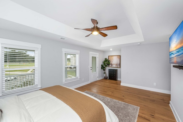 bedroom with hardwood / wood-style floors, ceiling fan, and a tray ceiling