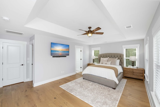 bedroom featuring ceiling fan, light wood-type flooring, and a tray ceiling