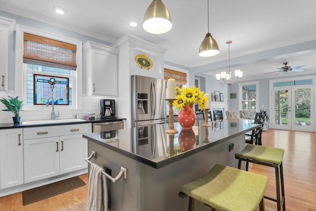 kitchen with ceiling fan with notable chandelier, a kitchen breakfast bar, stainless steel appliances, hanging light fixtures, and white cabinetry