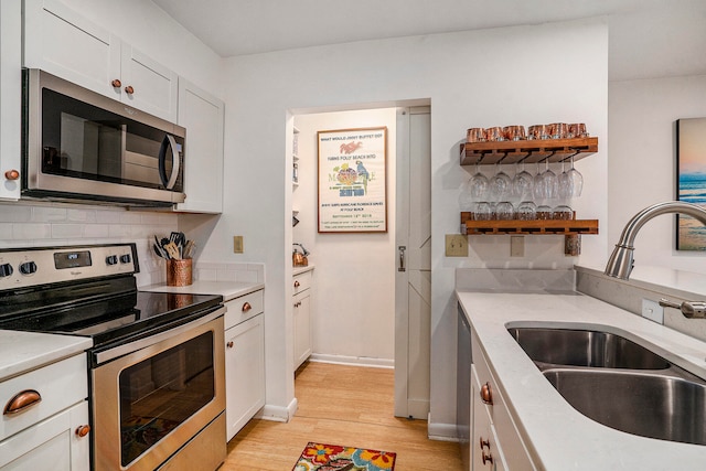 kitchen with backsplash, appliances with stainless steel finishes, sink, white cabinets, and light hardwood / wood-style flooring