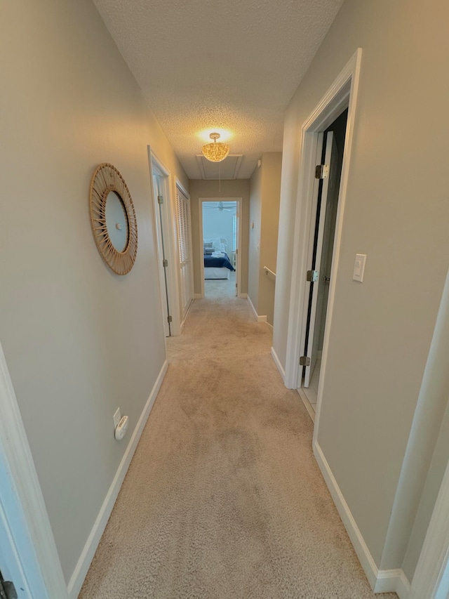 hall with a textured ceiling and light colored carpet