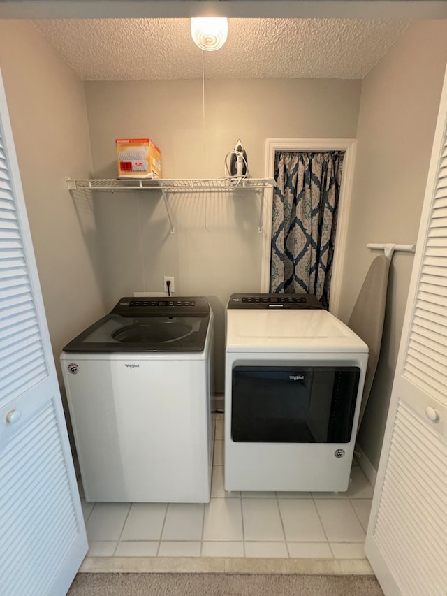 laundry room featuring a textured ceiling, separate washer and dryer, and light tile patterned floors