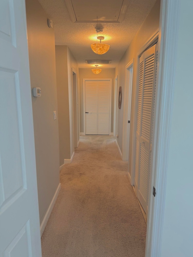 hallway with light carpet and a textured ceiling