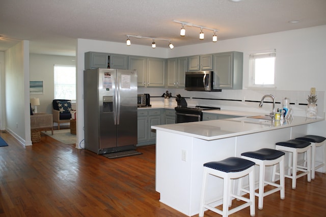 kitchen with sink, appliances with stainless steel finishes, kitchen peninsula, and dark hardwood / wood-style flooring