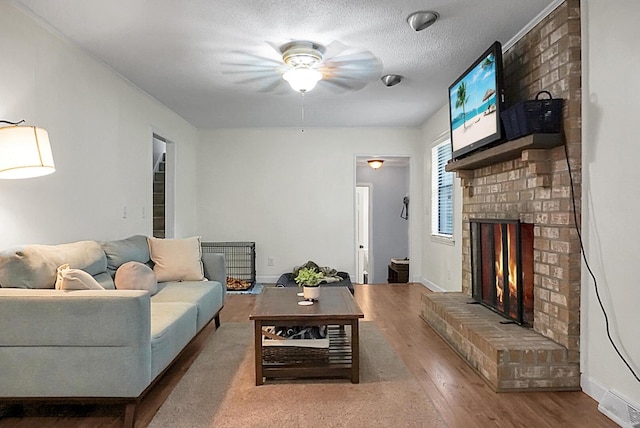 living room with a brick fireplace, ceiling fan, baseboards, and wood finished floors
