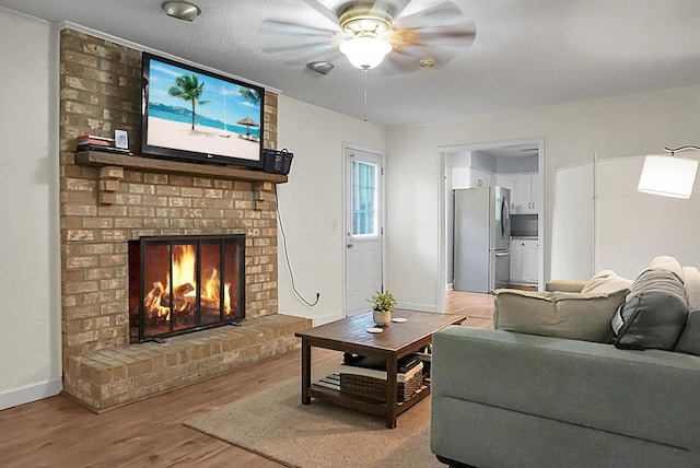 living area featuring light wood-style floors, baseboards, a ceiling fan, and a brick fireplace