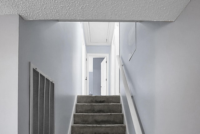 stairs featuring a heating unit, a textured ceiling, and attic access