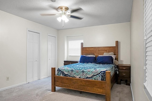 carpeted bedroom featuring baseboards, a ceiling fan, multiple closets, and a textured ceiling