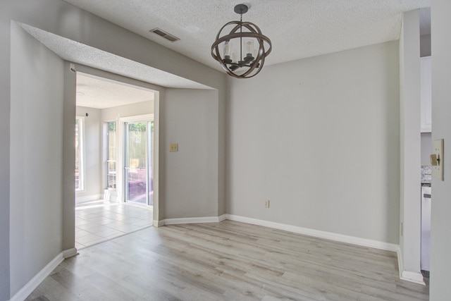 unfurnished dining area with visible vents, baseboards, light wood-style flooring, a textured ceiling, and a notable chandelier