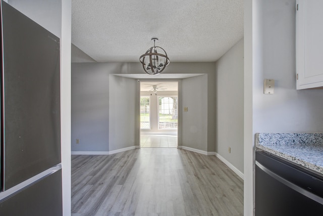 unfurnished dining area with ceiling fan with notable chandelier, light wood-style flooring, baseboards, and a textured ceiling
