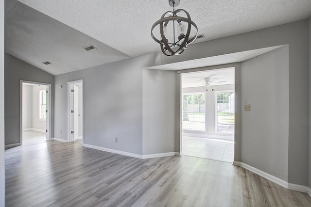 empty room featuring vaulted ceiling, visible vents, wood finished floors, a textured ceiling, and ceiling fan with notable chandelier