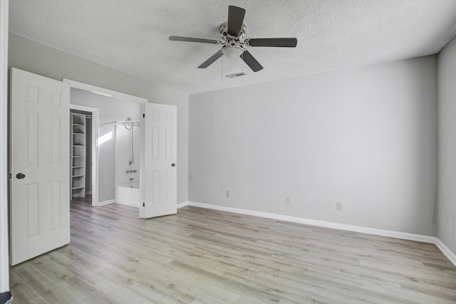 unfurnished bedroom with a spacious closet, visible vents, light wood-type flooring, baseboards, and a textured ceiling