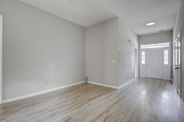 entryway with light wood-style floors, a textured ceiling, and baseboards