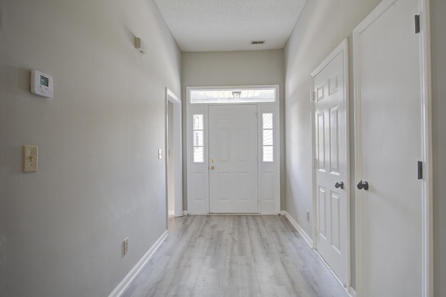 entryway with a textured ceiling, light wood finished floors, baseboards, and visible vents