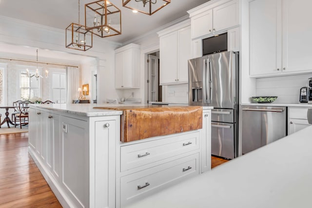 kitchen with a kitchen island, appliances with stainless steel finishes, decorative light fixtures, white cabinets, and light wood-type flooring