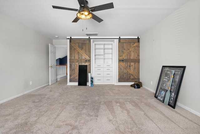 unfurnished living room with a barn door, ceiling fan, and carpet floors