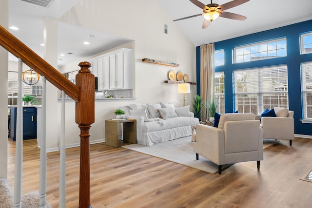 living room featuring light hardwood / wood-style floors, ceiling fan with notable chandelier, and high vaulted ceiling