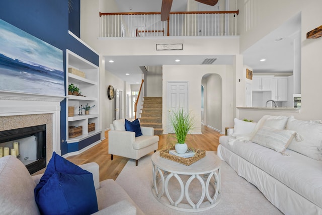 living room featuring built in features, a towering ceiling, sink, light hardwood / wood-style floors, and ceiling fan