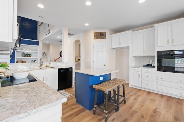 kitchen with a kitchen bar, a center island, white cabinets, black appliances, and sink