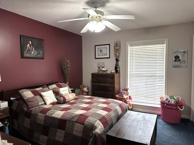 bedroom with dark colored carpet, a textured ceiling, and ceiling fan