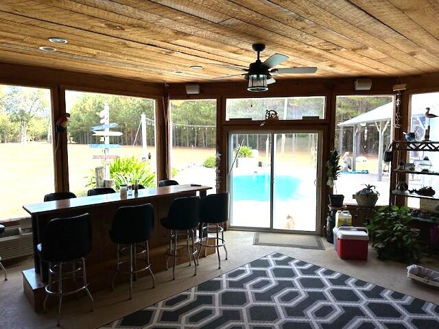 sunroom / solarium featuring bar area, ceiling fan, wooden ceiling, and a wealth of natural light