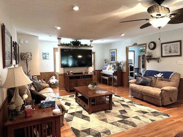 living room with light hardwood / wood-style floors, a textured ceiling, and ceiling fan