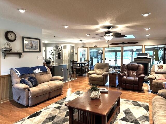 living room with ceiling fan, a skylight, and light wood-type flooring