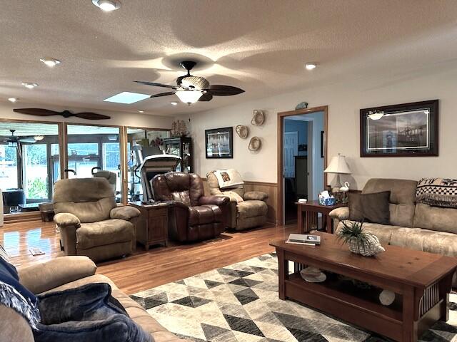 living room with ceiling fan, a textured ceiling, a skylight, and light wood-type flooring