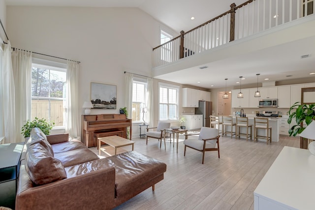 living area with light wood finished floors, visible vents, recessed lighting, and high vaulted ceiling