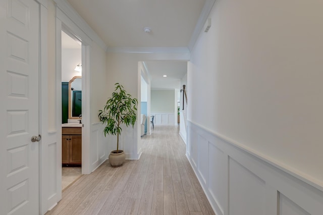 hallway with crown molding, a wainscoted wall, light wood-type flooring, a decorative wall, and a sink