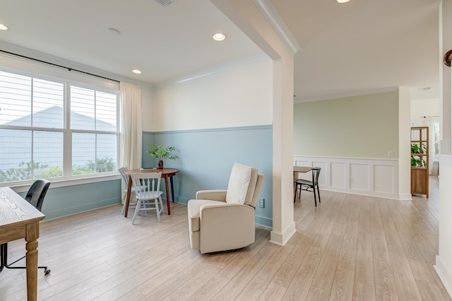 sitting room with a wainscoted wall, light wood finished floors, recessed lighting, crown molding, and a decorative wall