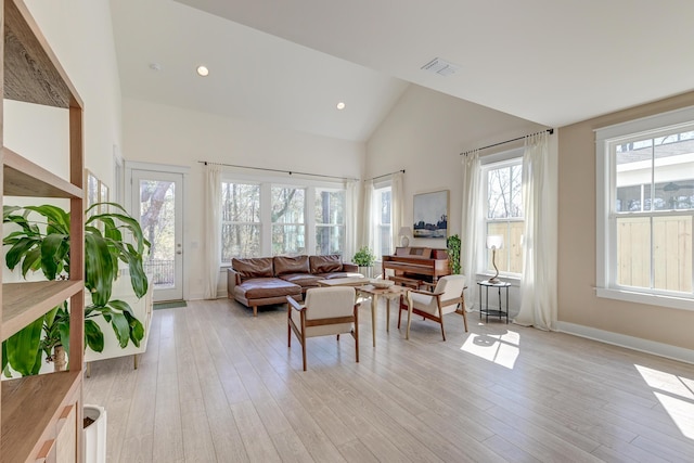 living area with light wood-type flooring, visible vents, baseboards, and high vaulted ceiling