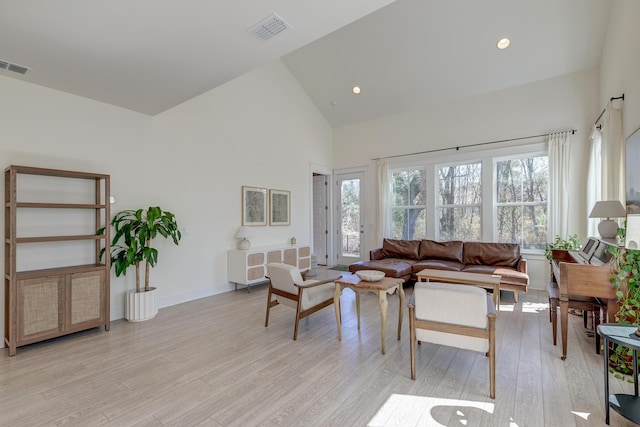 living room with visible vents, light wood-type flooring, a wealth of natural light, and high vaulted ceiling