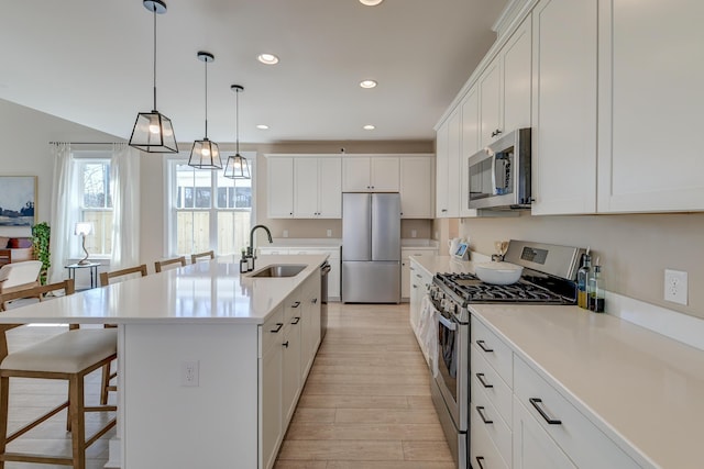 kitchen featuring light wood finished floors, a kitchen bar, recessed lighting, appliances with stainless steel finishes, and a sink