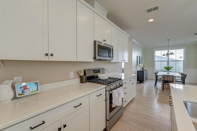 kitchen with a wainscoted wall, visible vents, ornamental molding, white cabinetry, and stainless steel appliances