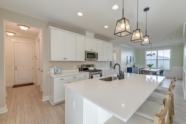 kitchen with a center island with sink, appliances with stainless steel finishes, light wood-style floors, and a sink