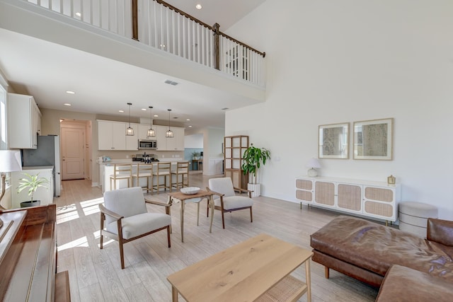 living room with visible vents, recessed lighting, light wood-style floors, a high ceiling, and baseboards