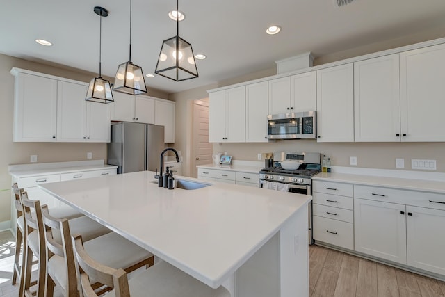 kitchen with light countertops, an island with sink, appliances with stainless steel finishes, light wood-style floors, and a sink