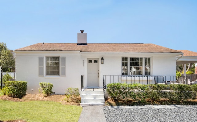 view of front of home featuring a front lawn, covered porch, roof with shingles, and a chimney