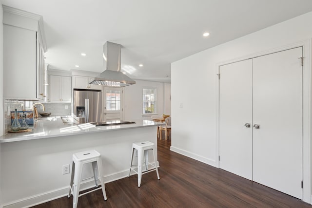 kitchen featuring a sink, decorative backsplash, light countertops, stainless steel refrigerator with ice dispenser, and island range hood