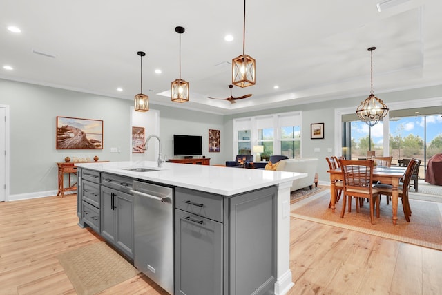 kitchen featuring dishwasher, sink, a raised ceiling, decorative light fixtures, and a kitchen island with sink