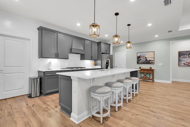 kitchen with gray cabinetry, stainless steel fridge with ice dispenser, premium range hood, an island with sink, and pendant lighting