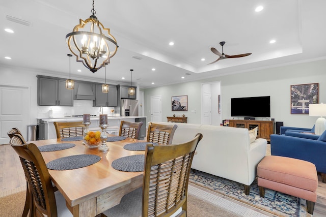 dining space featuring a raised ceiling, crown molding, ceiling fan with notable chandelier, and light wood-type flooring